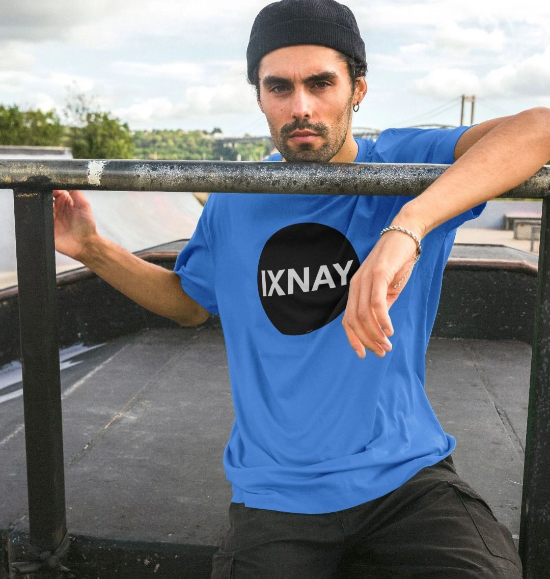 Man at skate park wearing bright blue  Printed Men's T-Shirt with Original Black Round IXNAY Logo to represent the artist and musician IXNAY