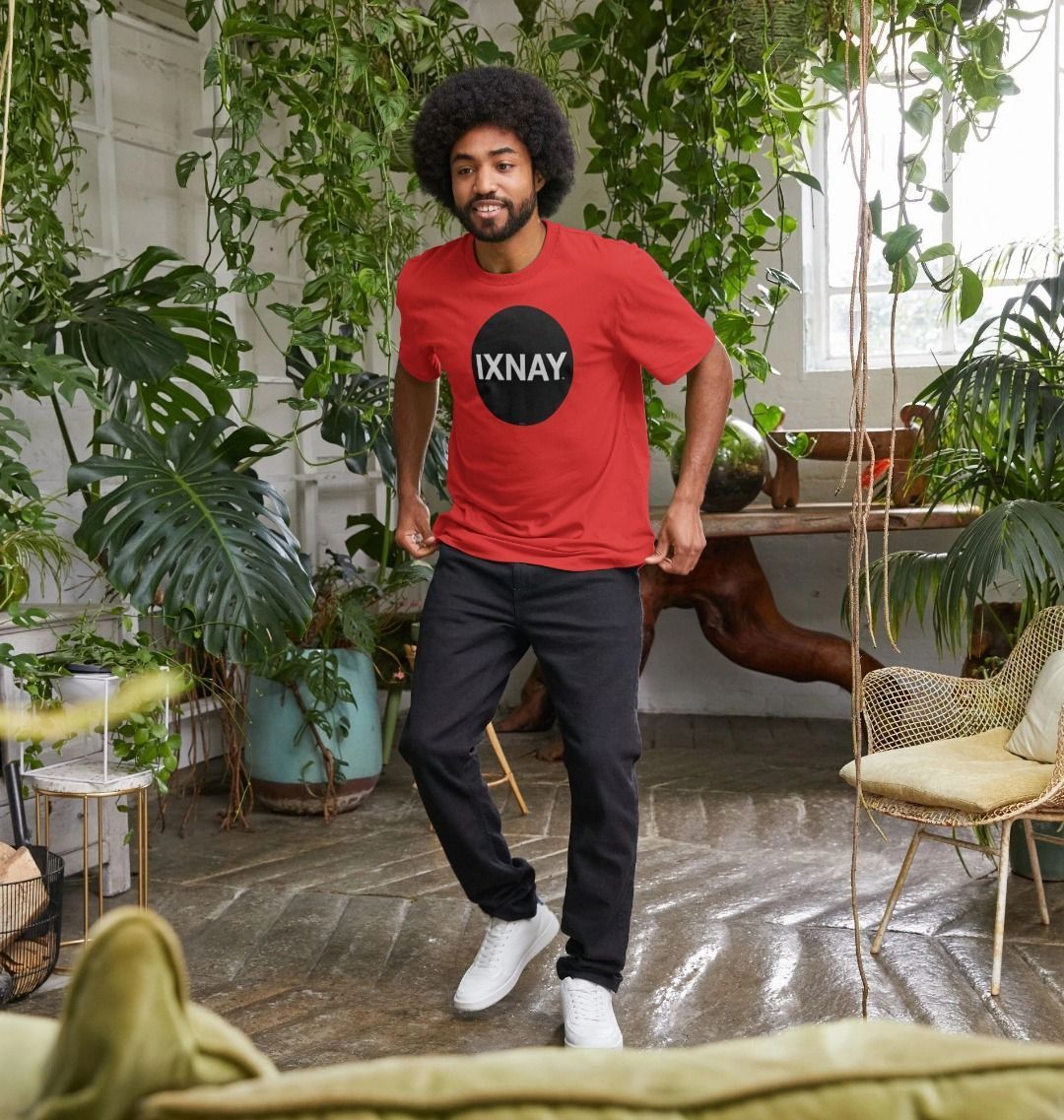 Smiling black man in loft-style room with many plants and sunshine wearing a bright red Printed Men's T-Shirt with Original Black Round IXNAY Logo to represent the artist and musician IXNAY