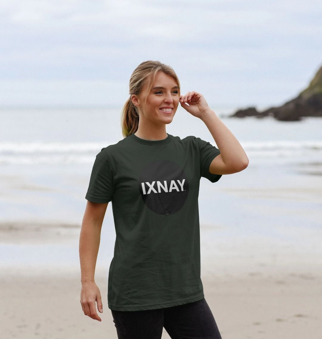 Woman smiling on the beach wearing a dark gray Printed Men's T-Shirt with Original Black Round IXNAY Logo to represent the artist and musician IXNAY