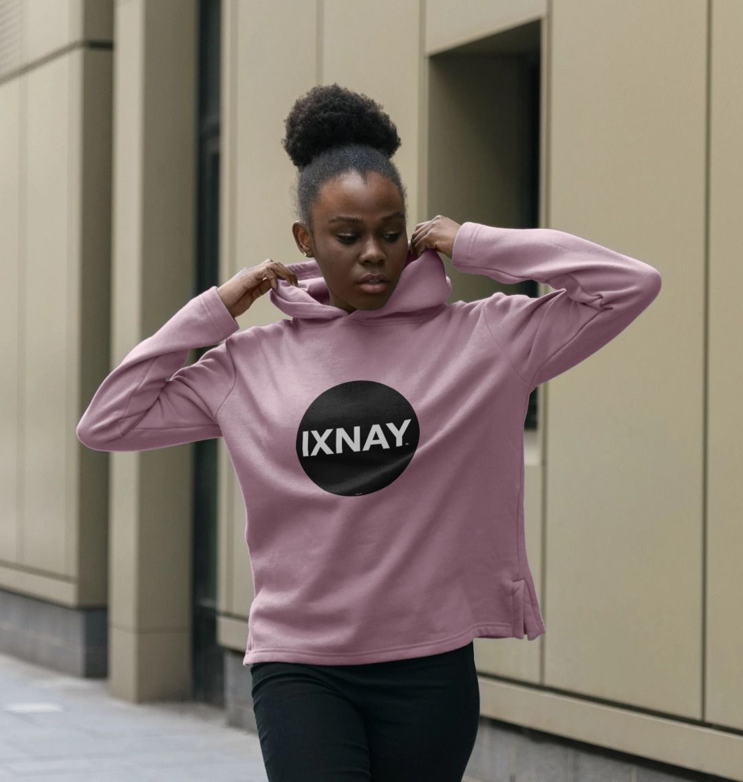 black woman on city street wearing womens mauve pink organic pullover hoodie with original black round IXNAY logo